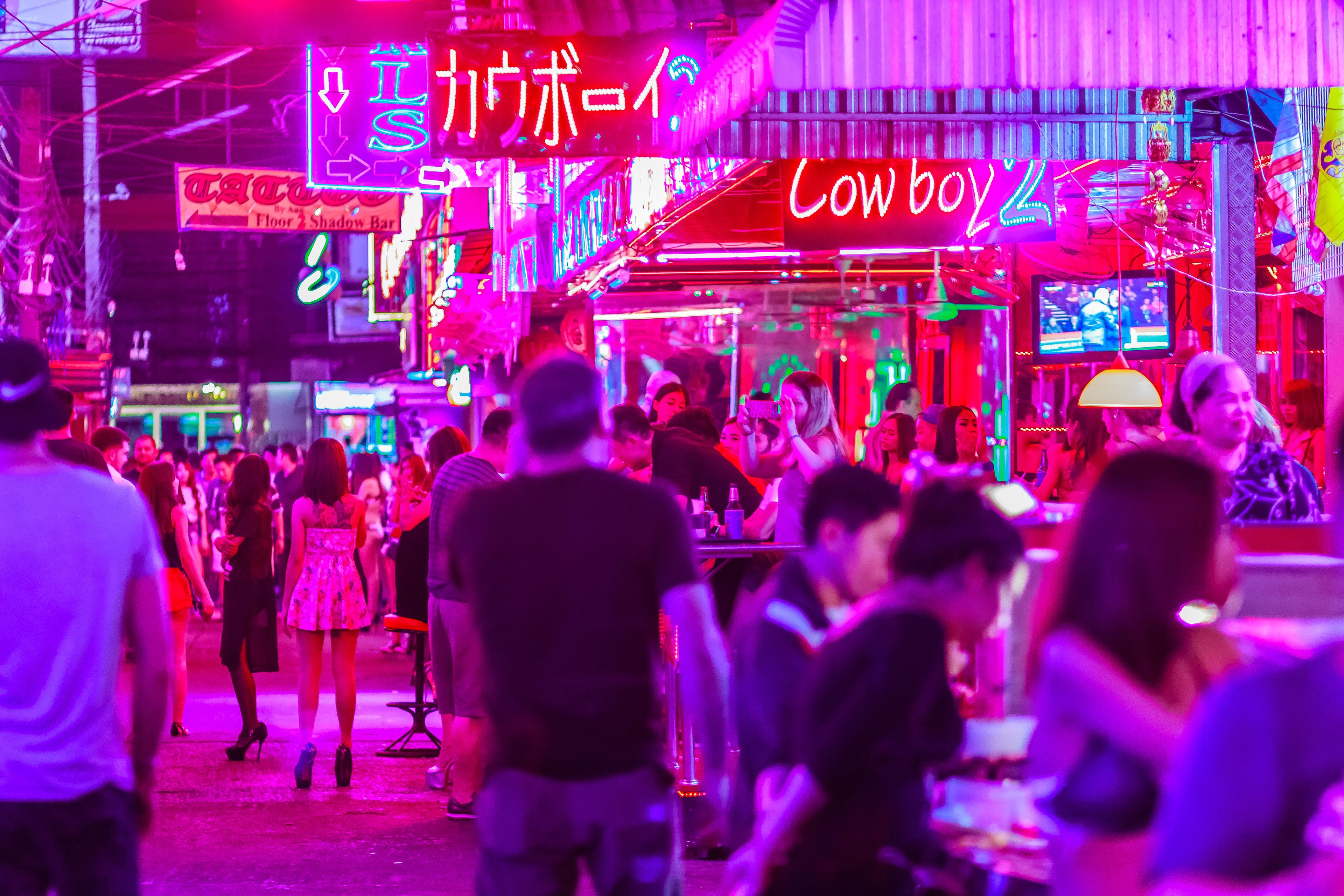 A crowded street with neon signs and a bar.