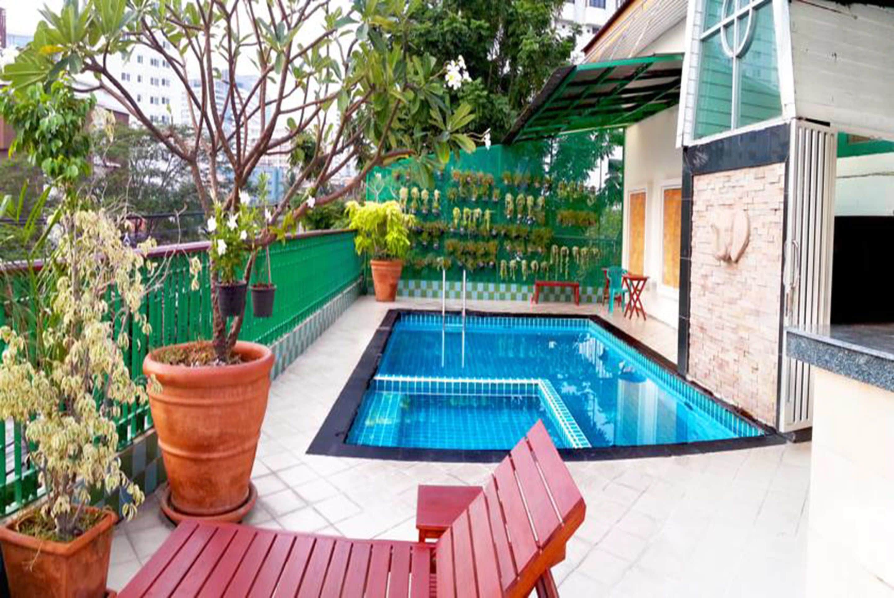 A swimming pool with a tiled deck, surrounded by potted plants and a green fence.