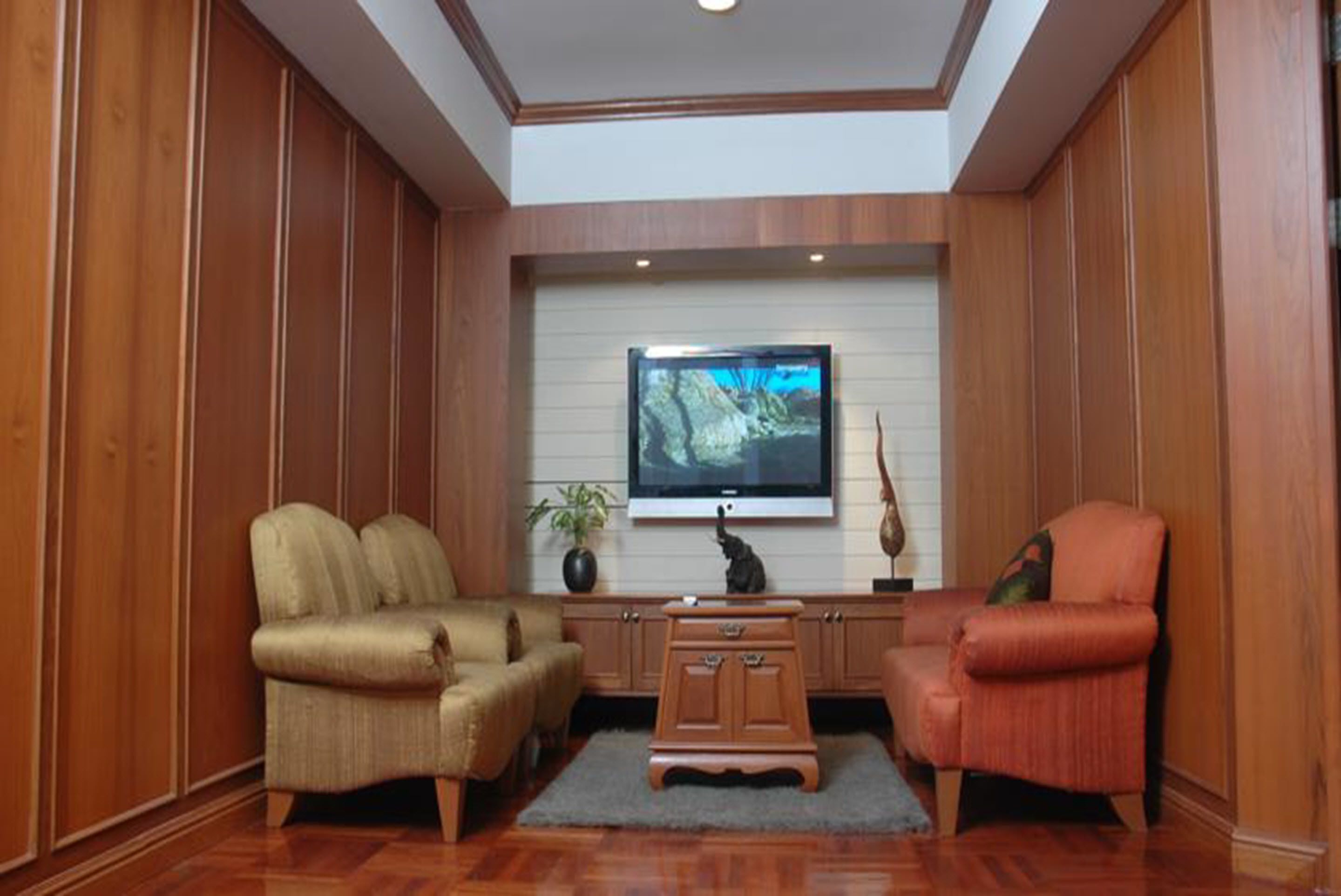 A living room with a flat-screen TV mounted on a wall, two sofas, a coffee table, and a decorative plant.