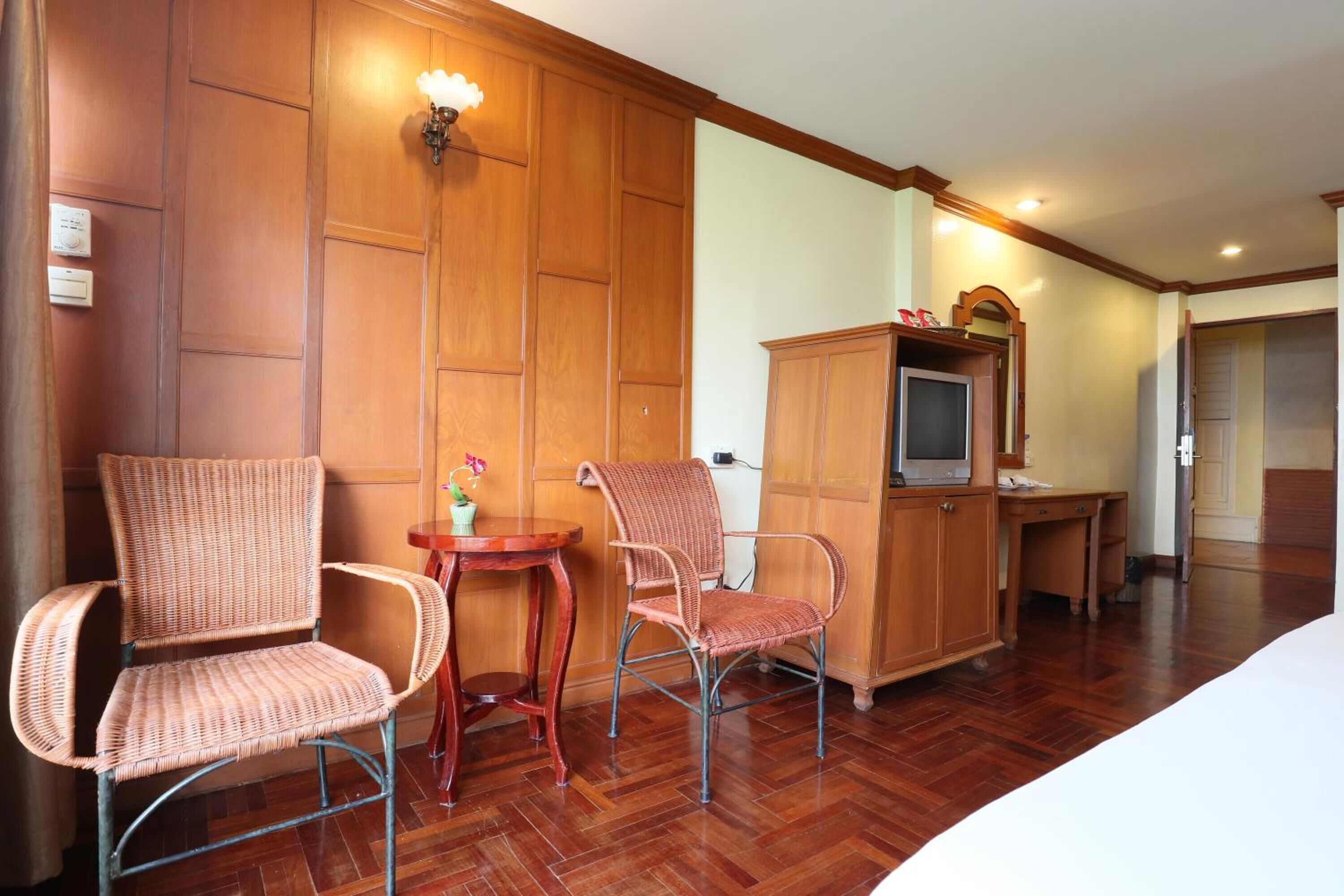 A hotel room with two wicker chairs, a small wooden table, a television on a cabinet, and a bed.