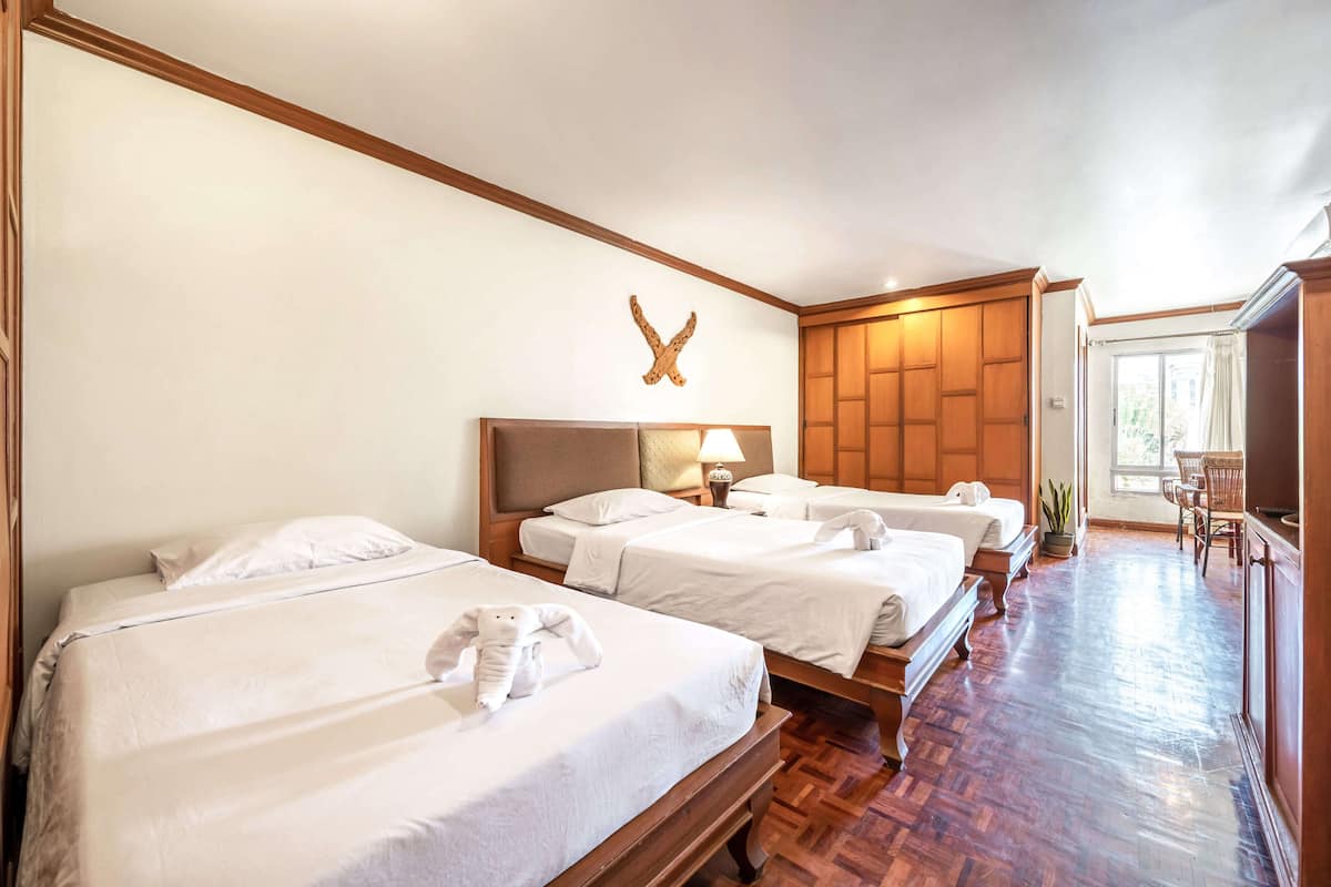 Une chambre d’hôtel avec trois lits, des têtes de lit en bois, une grande fenêtre et un plancher en bois.