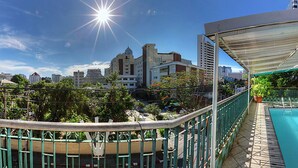 A rooftop pool with a glass balustrade, a covered seating area, and a view of the city skyline.