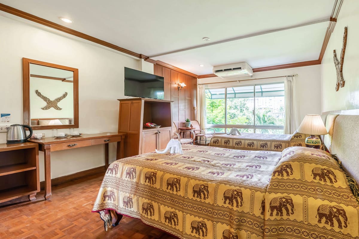 Une chambre à coucher avec un lit, un bureau en bois, une télévision et une fenêtre donnant sur un paysage verdoyant.