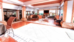 A spacious indoor area with a high ceiling, tiled floor, and multiple seating arrangements.