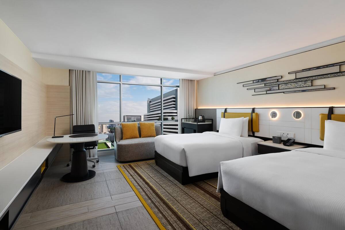 Une chambre d’hôtel avec deux lits, un bureau, une télévision et une vue sur le paysage urbain.