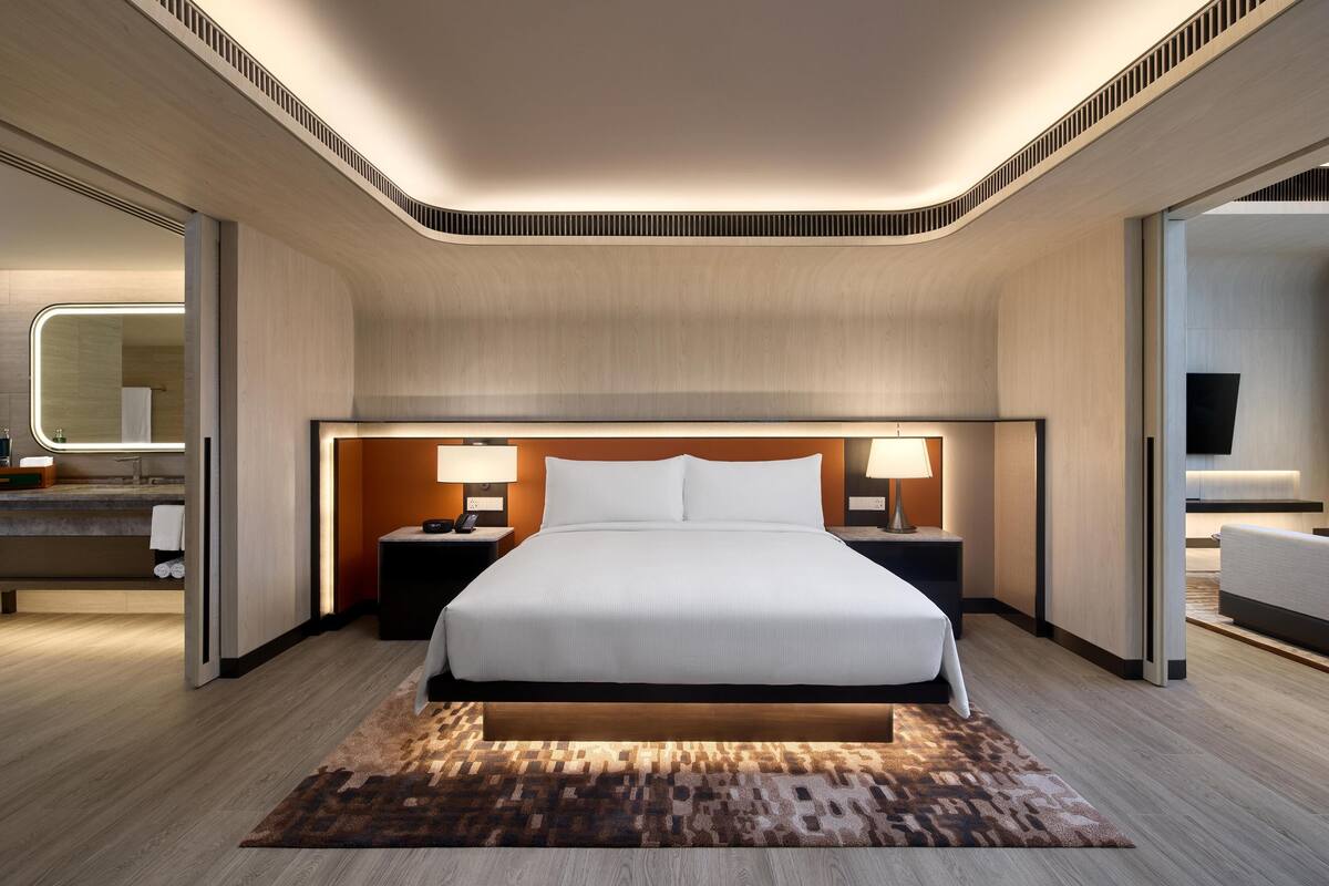 Une chambre d’hôtel moderne avec un grand lit, des tables de chevet avec des lampes, un miroir et une vue sur la salle de bain.