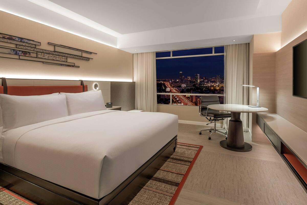 Une chambre d’hôtel avec un grand lit, un bureau, une chaise, une télévision et une vue sur la ville.