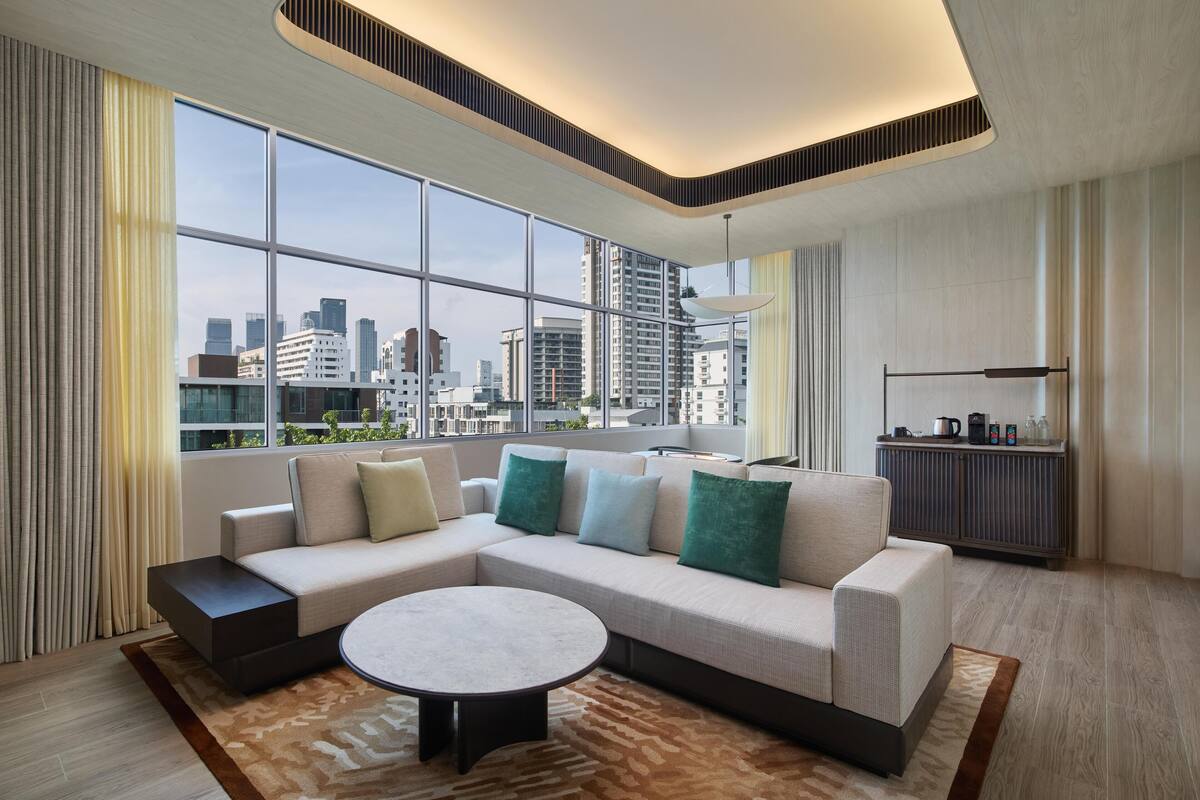 Un salon moderne avec un canapé d’angle, une table basse ronde et une vue sur la ville grâce à de grandes fenêtres.