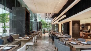 Een modern restaurant met lange tafels, comfortabele zitplaatsen en uitzicht op groen.