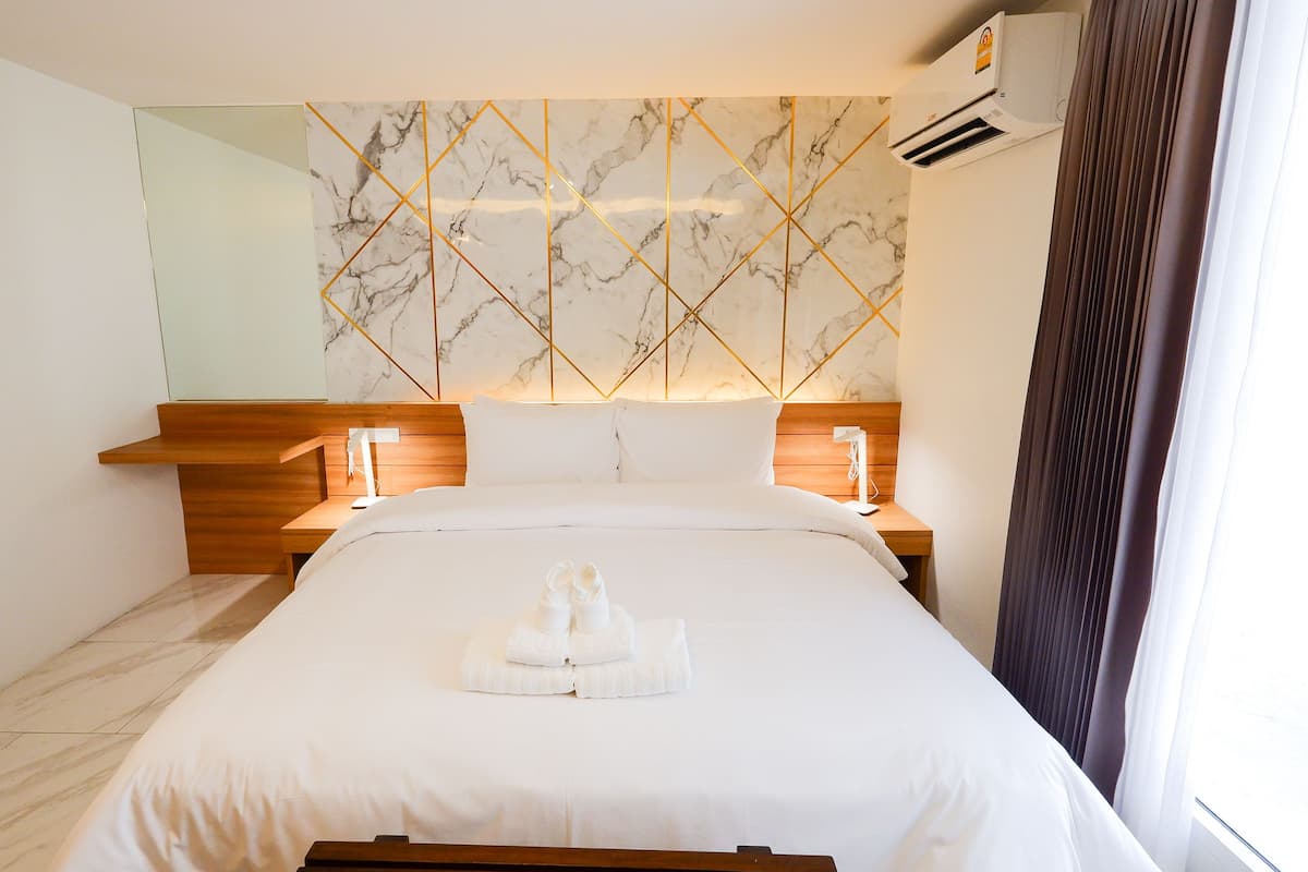 A hotel room with a marble-patterned wall, a wooden headboard, a bed with white linens, and a nightstand with a lamp.