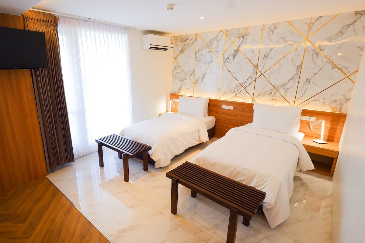 A hotel room with two beds, a TV, an air conditioner, and a marble-patterned wall.