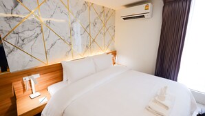 Une chambre d’hôtel avec un mur décoré d’un motif imitant le marbre, une tête de lit en bois, un lit avec du linge de maison blanc et un appareil de climatisation.