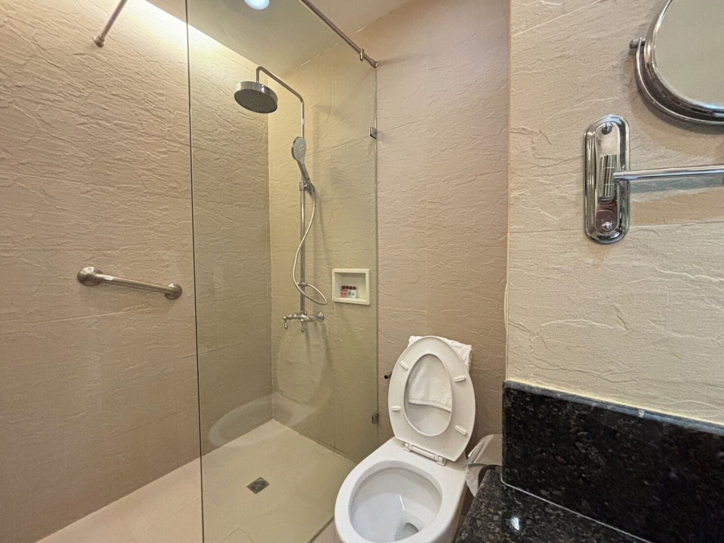 A modern bathroom with a glass-enclosed shower, a toilet, and a marble countertop.