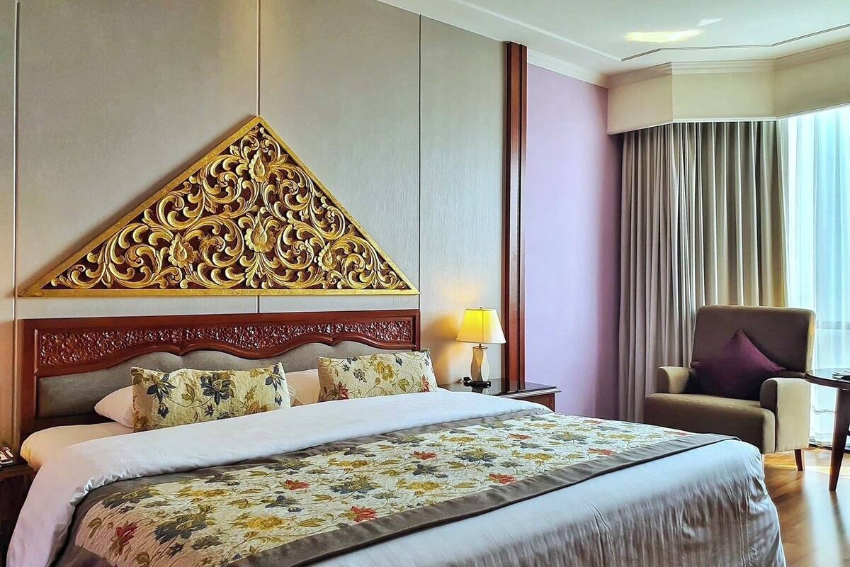 Quarto de hotel com uma cama grande, cabeceira decorativa, uma cadeira e um abajur.