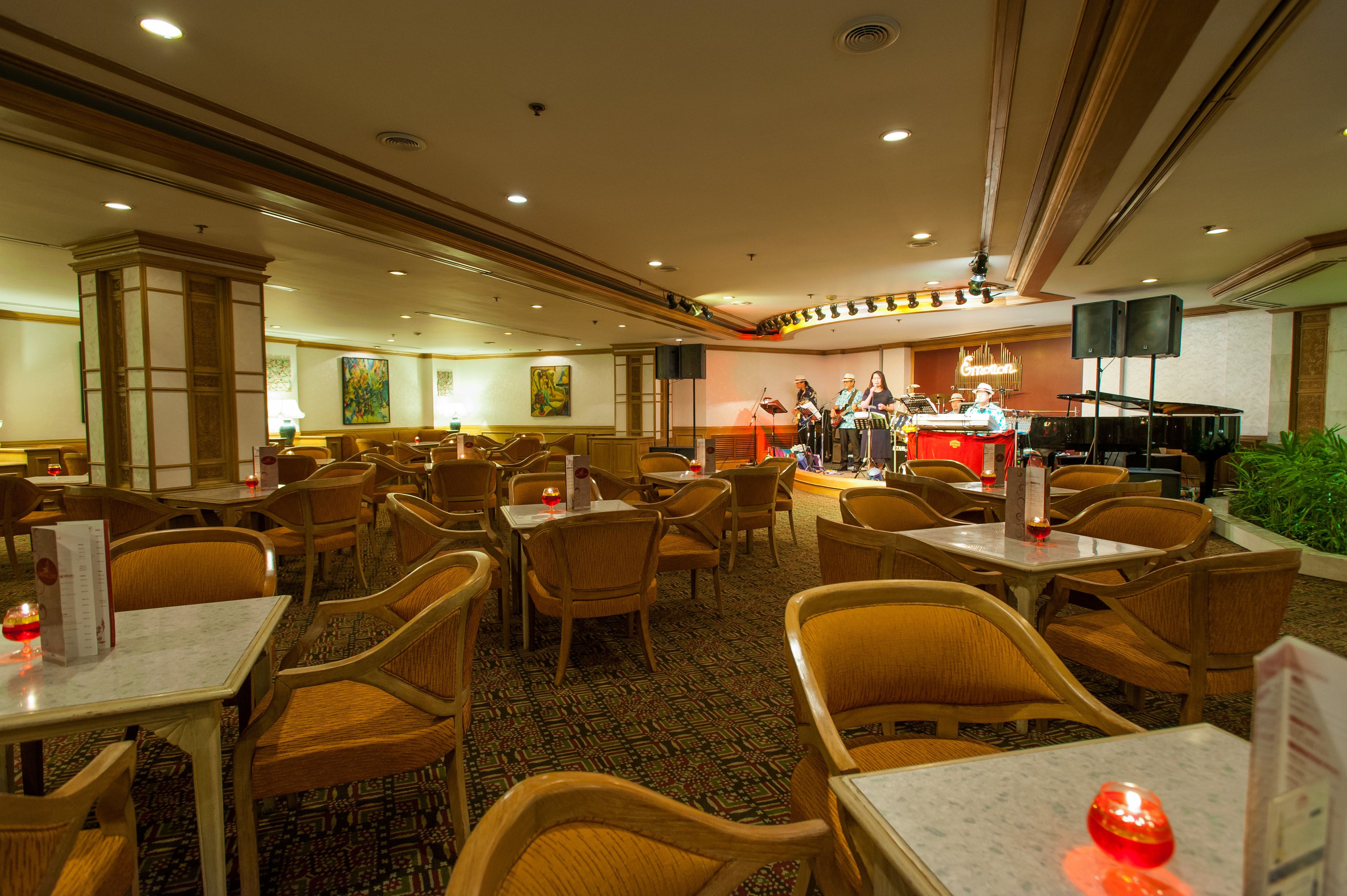 A spacious hotel lobby with multiple seating areas, a stage with musical equipment, and a bar.