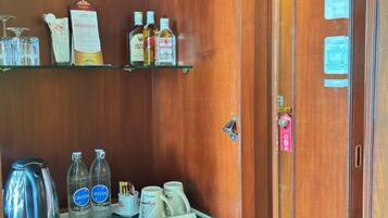 Habitación de hotel con puerta de madera, un mini bar con bebidas, una tetera y un refrigerador pequeño.