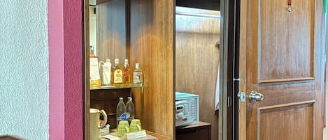 A hotel room with a wooden door labeled "301", a minibar with various bottles, a small refrigerator, and a patterned carpet.