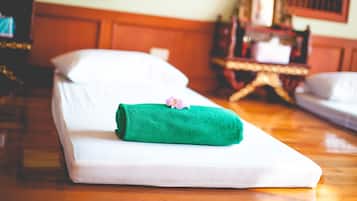 A neatly made bed with a green towel and a small flower on it, set in a room with wooden furniture and a mirror on the wall.