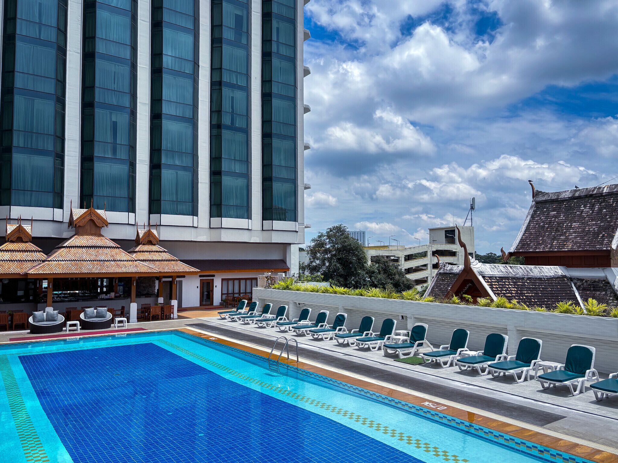 A swimming pool with lounge chairs and a restaurant area with traditional roof designs.