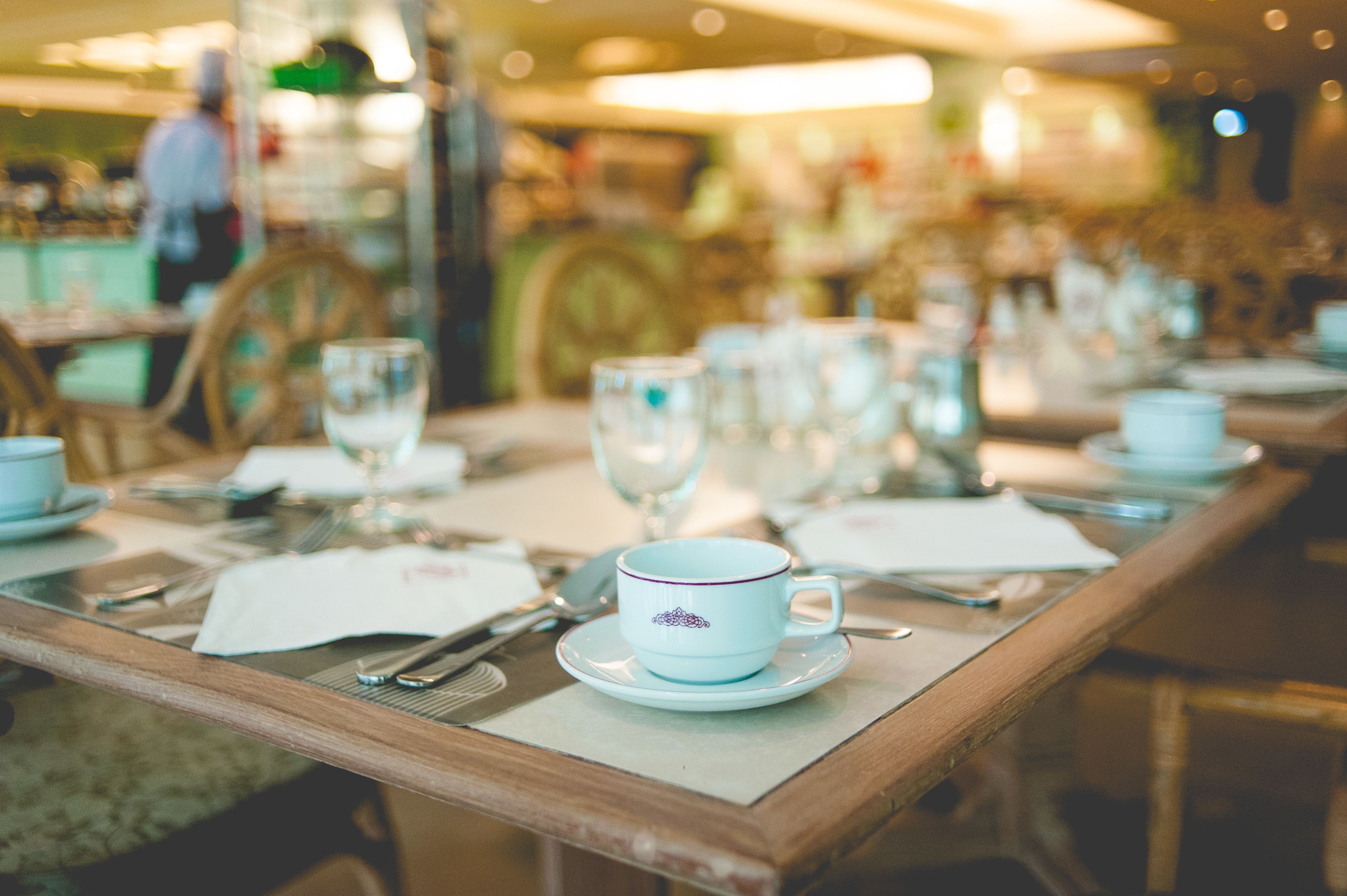 A dining table set with white plates, silverware, and a blue cup with a purple design.