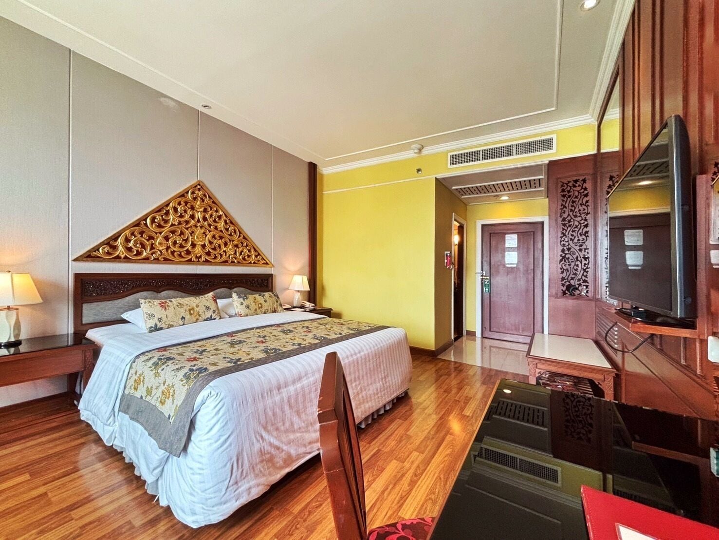 A hotel room with a large bed, wooden flooring, a TV, and a desk.