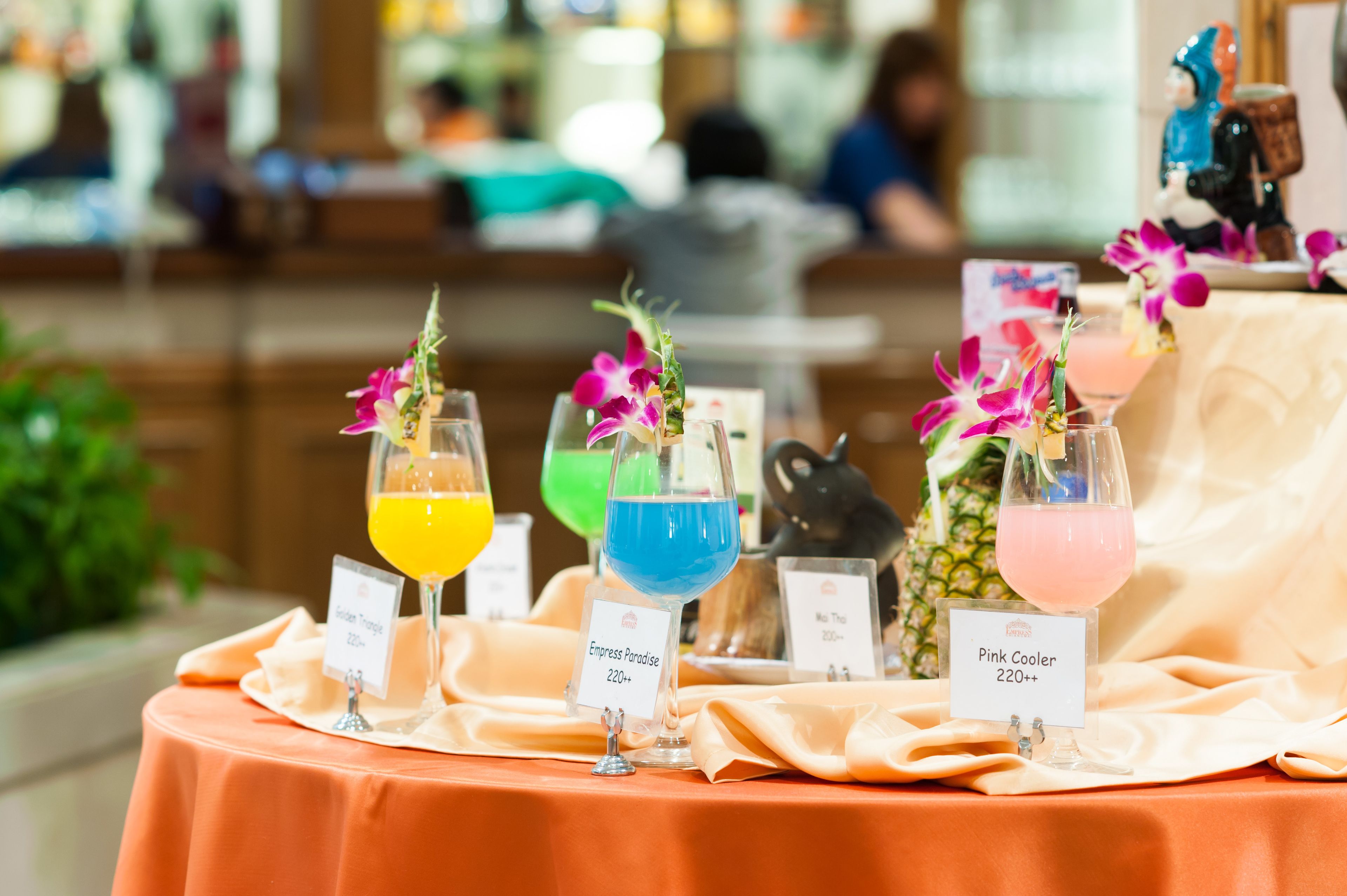 A table with three drinks labeled 'Empress Paradise' and 'Pink Cooler', each with a floral garnish.