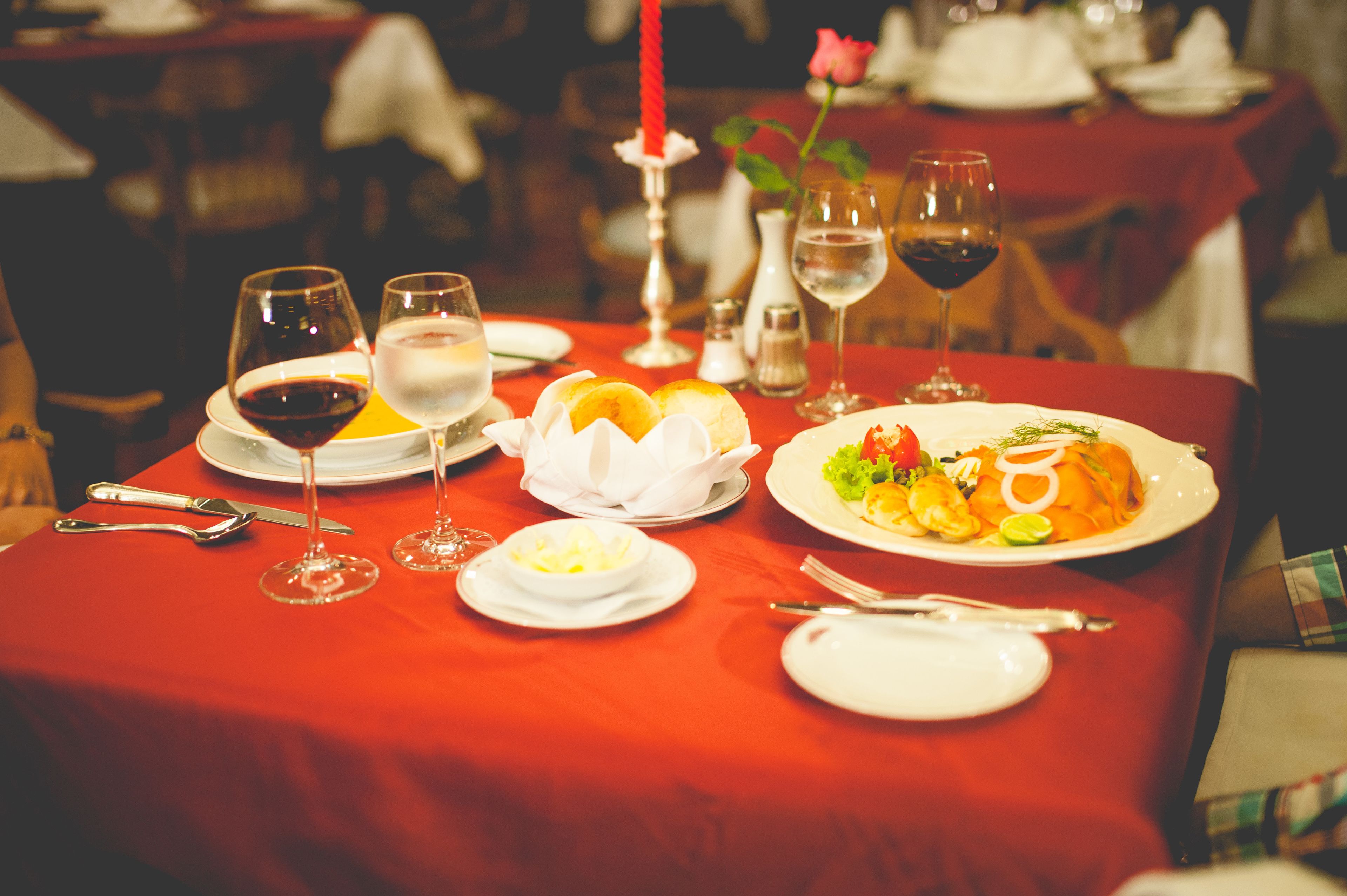 A dining table set with plates, glasses, and cutlery, with a red tablecloth and a candle centerpiece.