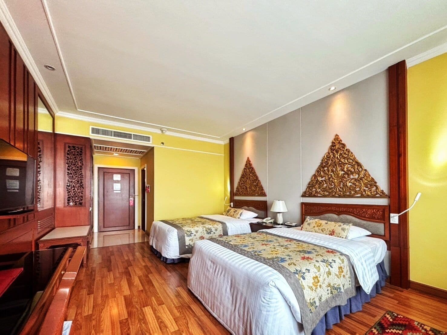 A hotel room with two beds, wooden flooring, a television, and decorative wall panels.