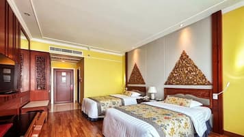 A hotel room with two beds, wooden flooring, a television, and decorative wall panels.