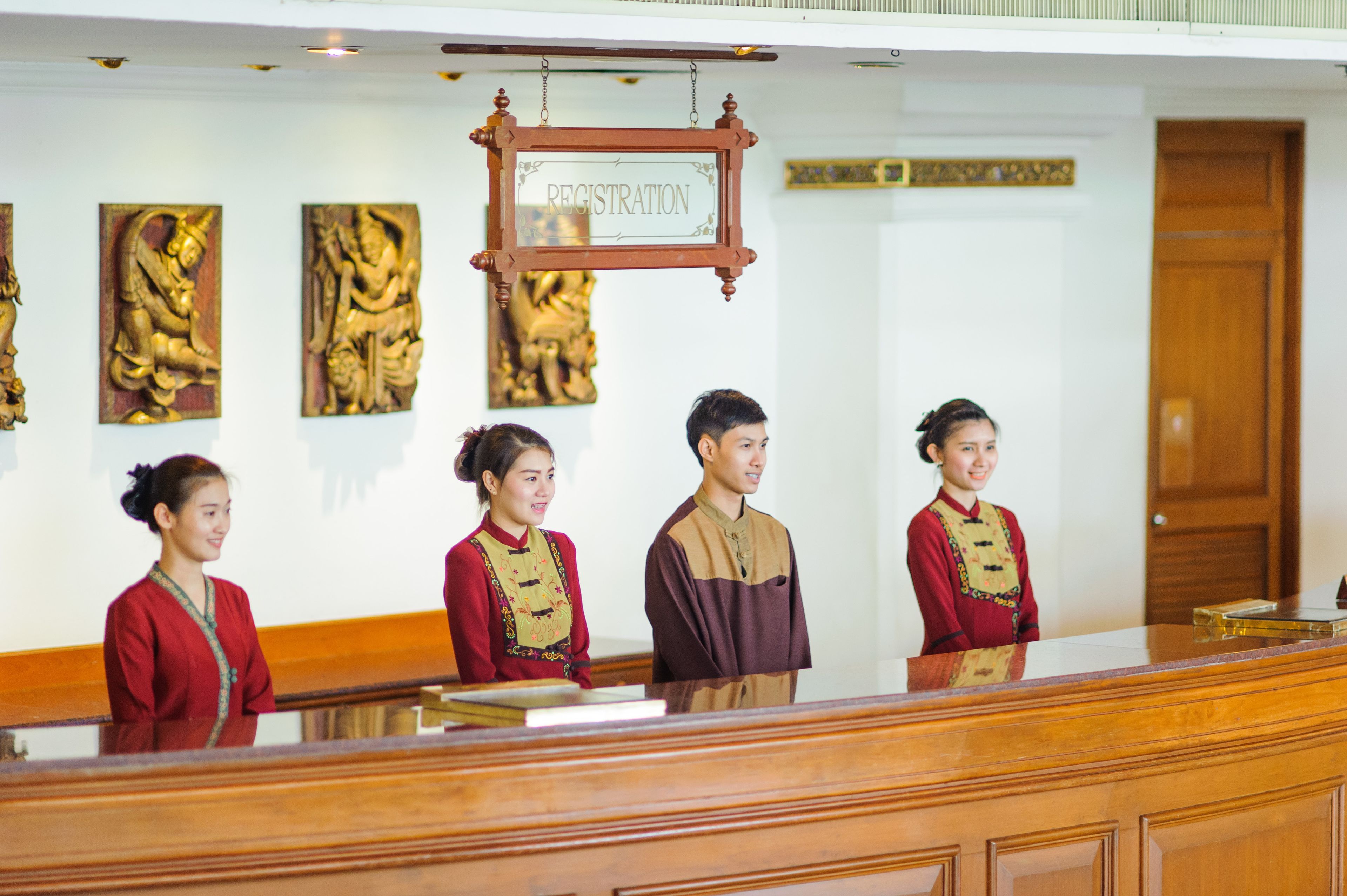 A reception desk with a registration sign, three staff members in traditional attire, and cultural artwork on the wall.