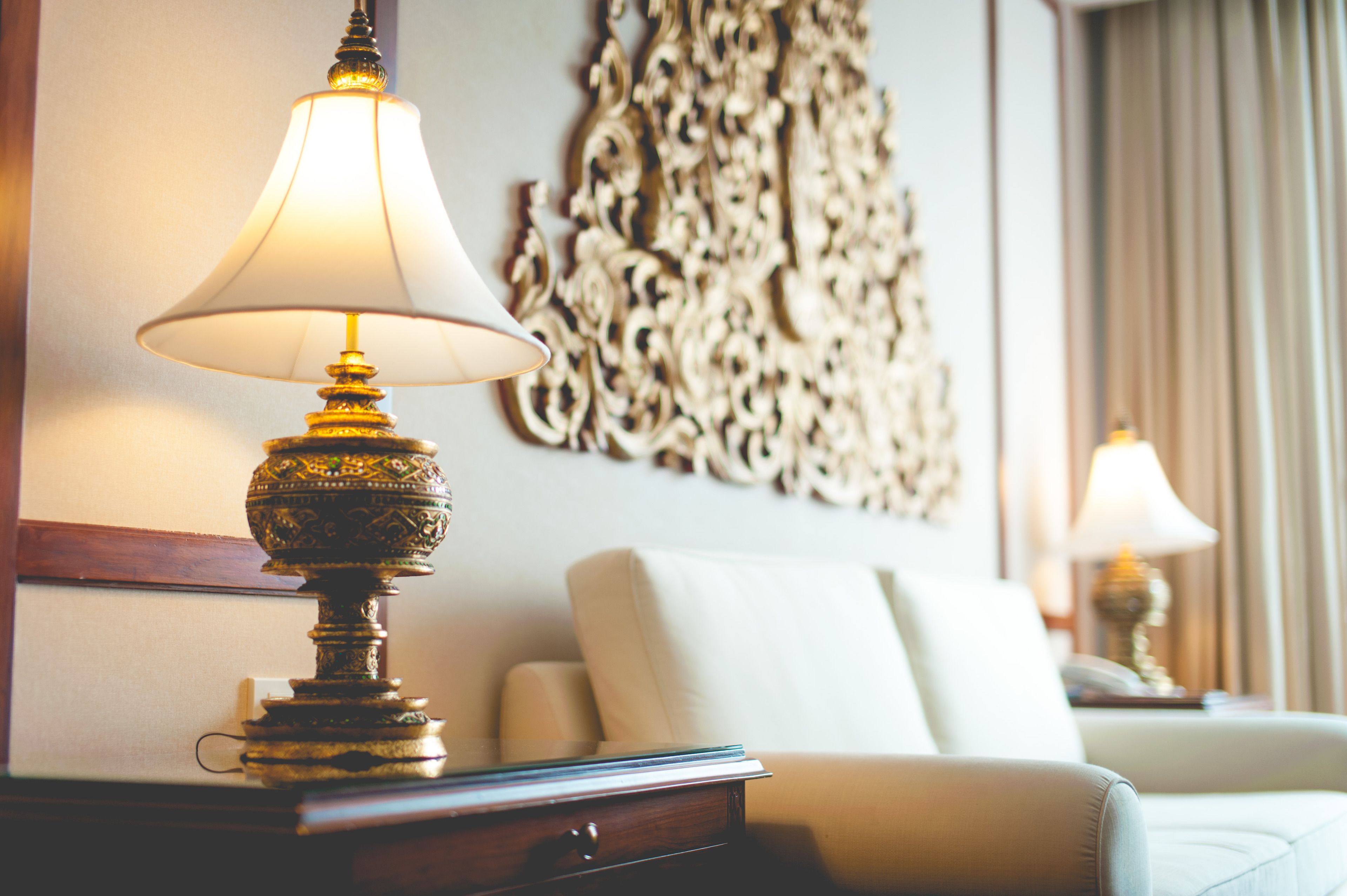 Una lámpara con pantalla blanca sobre una mesa de madera, un sofá color beige y un adorno decorativo en una habitación de hotel.