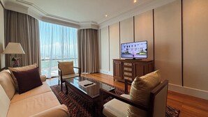 Une chambre d’hôtel moderne dotée d’une grande fenêtre, d’un canapé, d’un fauteuil, d’une table basse et d’un téléviseur.