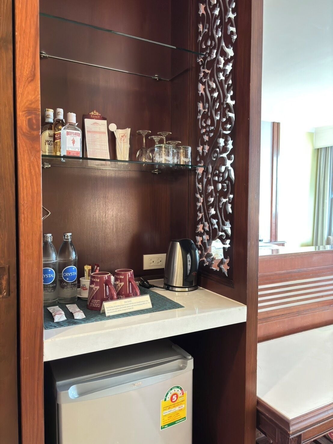 Un minibar compacto con refrigerador, cafetera y diferentes bebidas y condimentos.