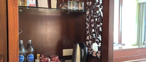 Un minibar compacto con refrigerador, cafetera y diferentes bebidas y condimentos.