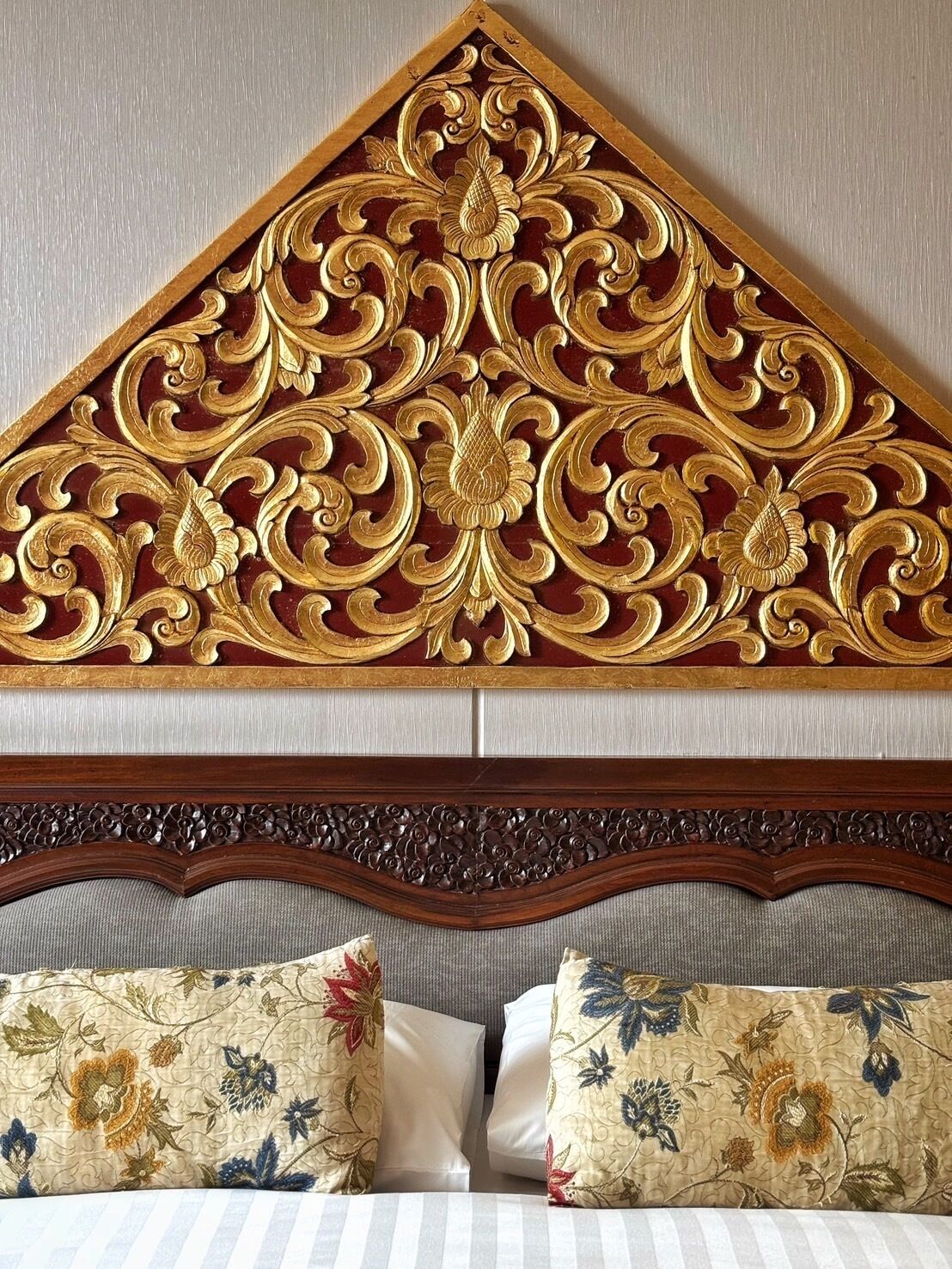A bed with a wooden headboard featuring intricate carvings and floral-patterned pillows.