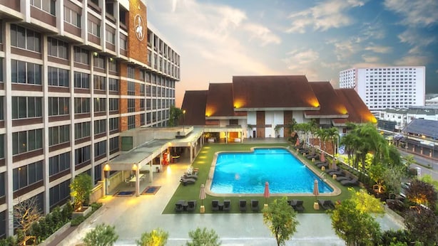 Un hotel con piscina, mobiliario exterior y un edificio grande con una torre del reloj.
