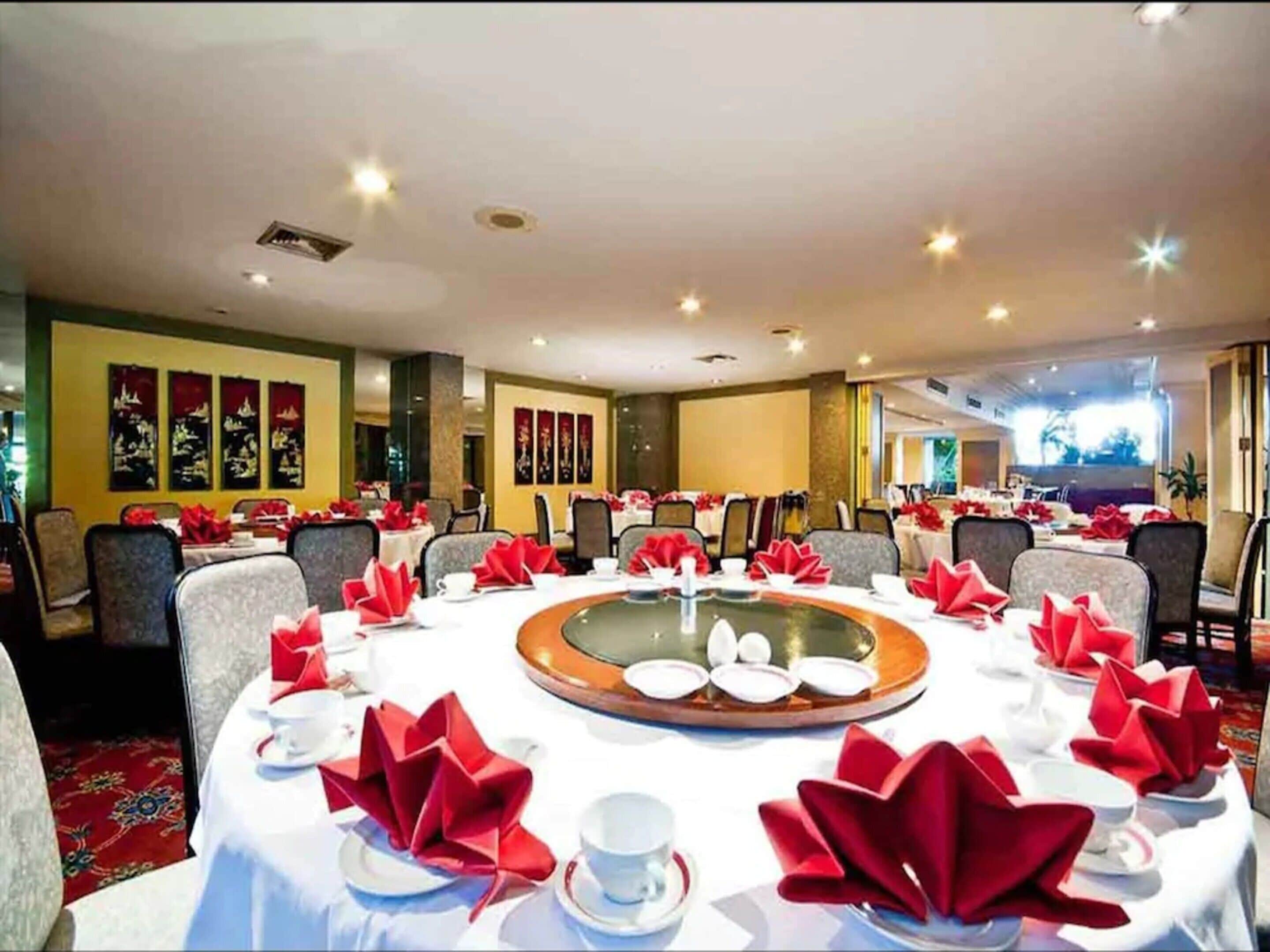 Une salle de banquet avec des tables rondes dressées pour un événement formel, agr émentée de serviettes rouges et de vaisselle blanche.