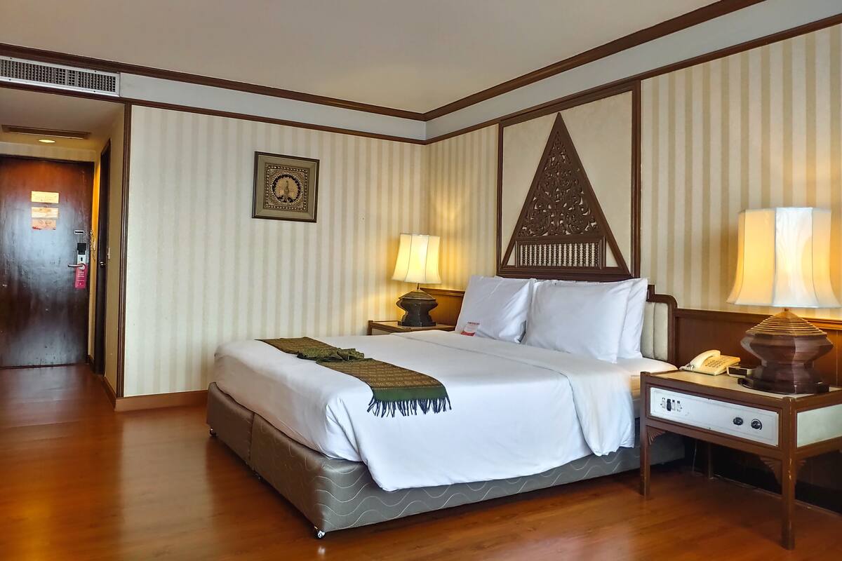 Ein Hotelzimmer mit einem großen Bett, zwei Nachttischen mit Lampen, einem Holz-Kopfteil und einer gestreiften Wand.