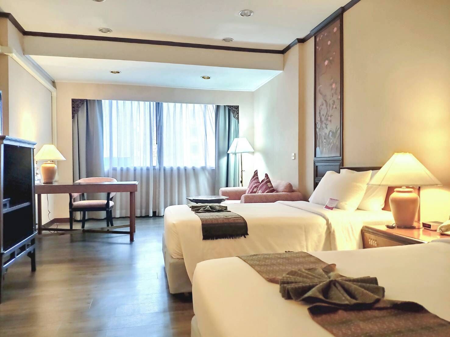 A hotel room with two beds, a desk, a chair, and a TV.