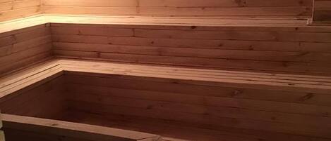 A wooden sauna with a bench and a small table.