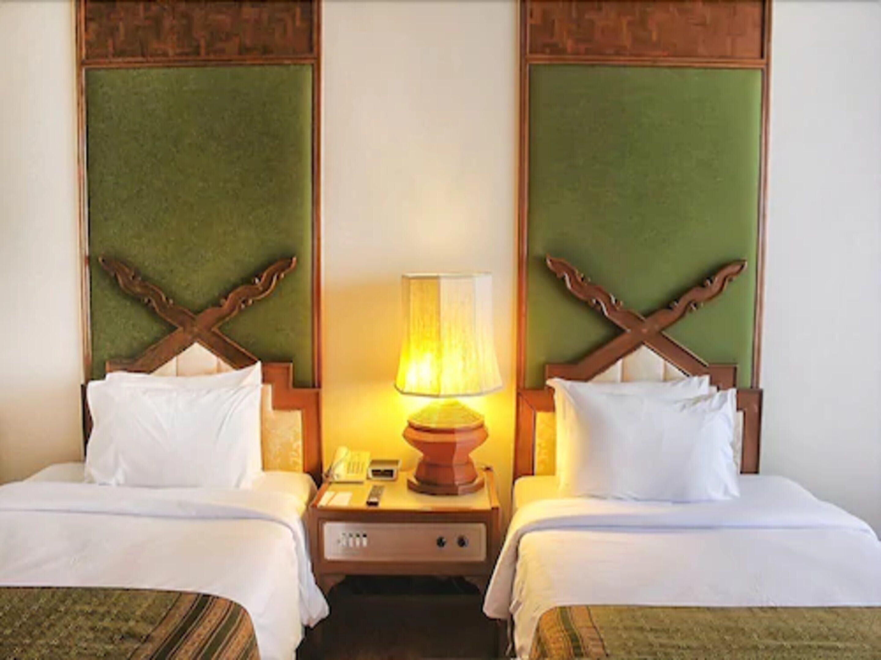 A hotel room with two beds, a nightstand with a lamp, and a telephone.