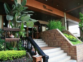 Entrada de hotel con una escalera que conduce al edificio principal, rodeada de abundante vegetación y una mesa decorativa.