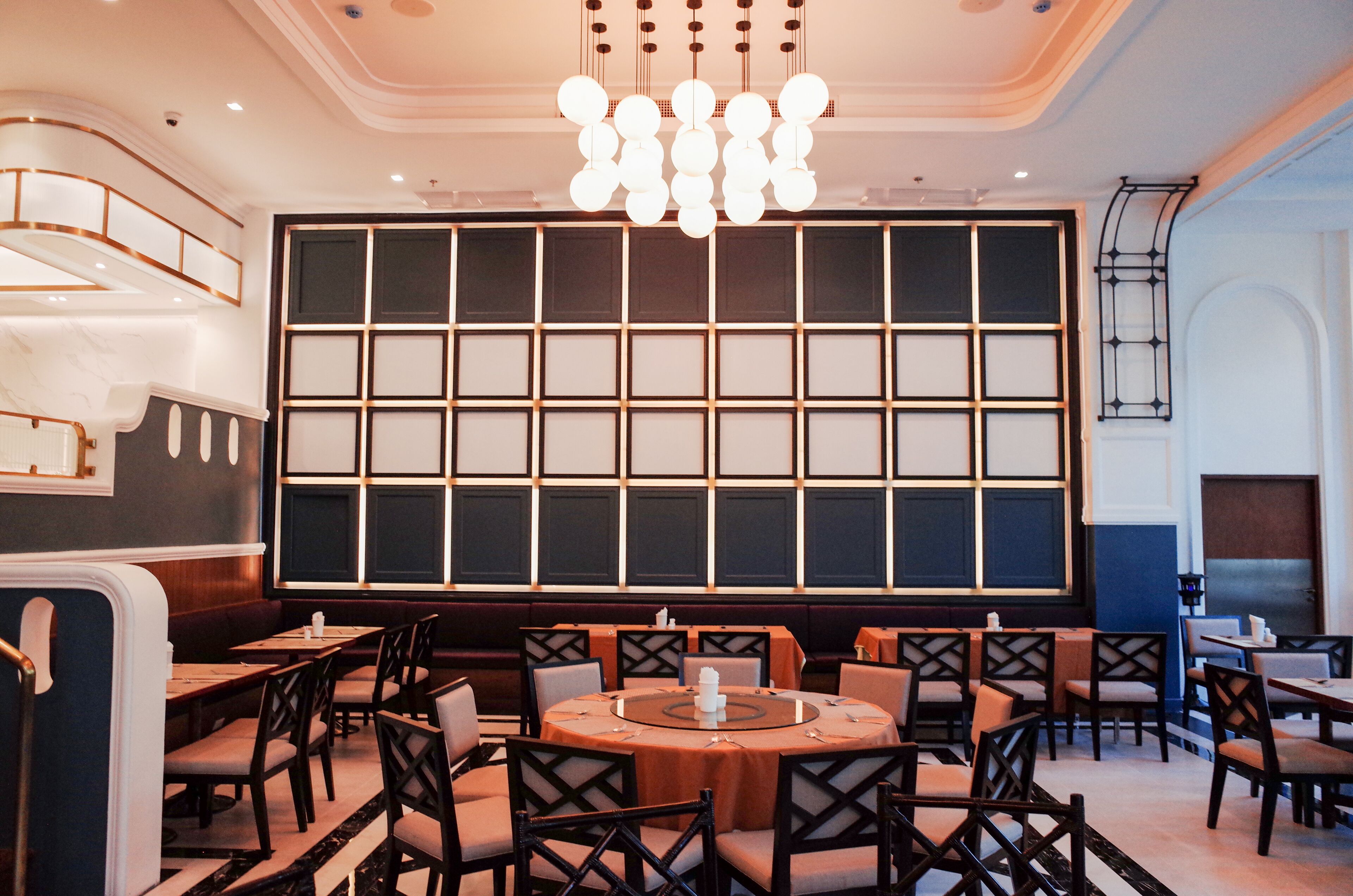A dining area with round tables, chairs, and a large wall with a grid pattern.