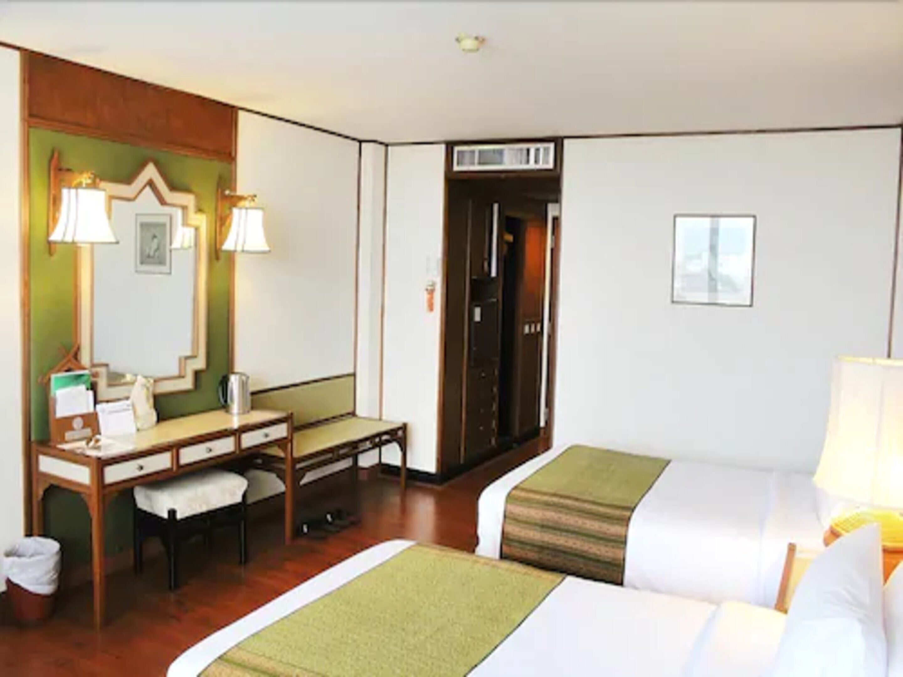 A hotel room with two beds, a desk, a chair, and a mirror.