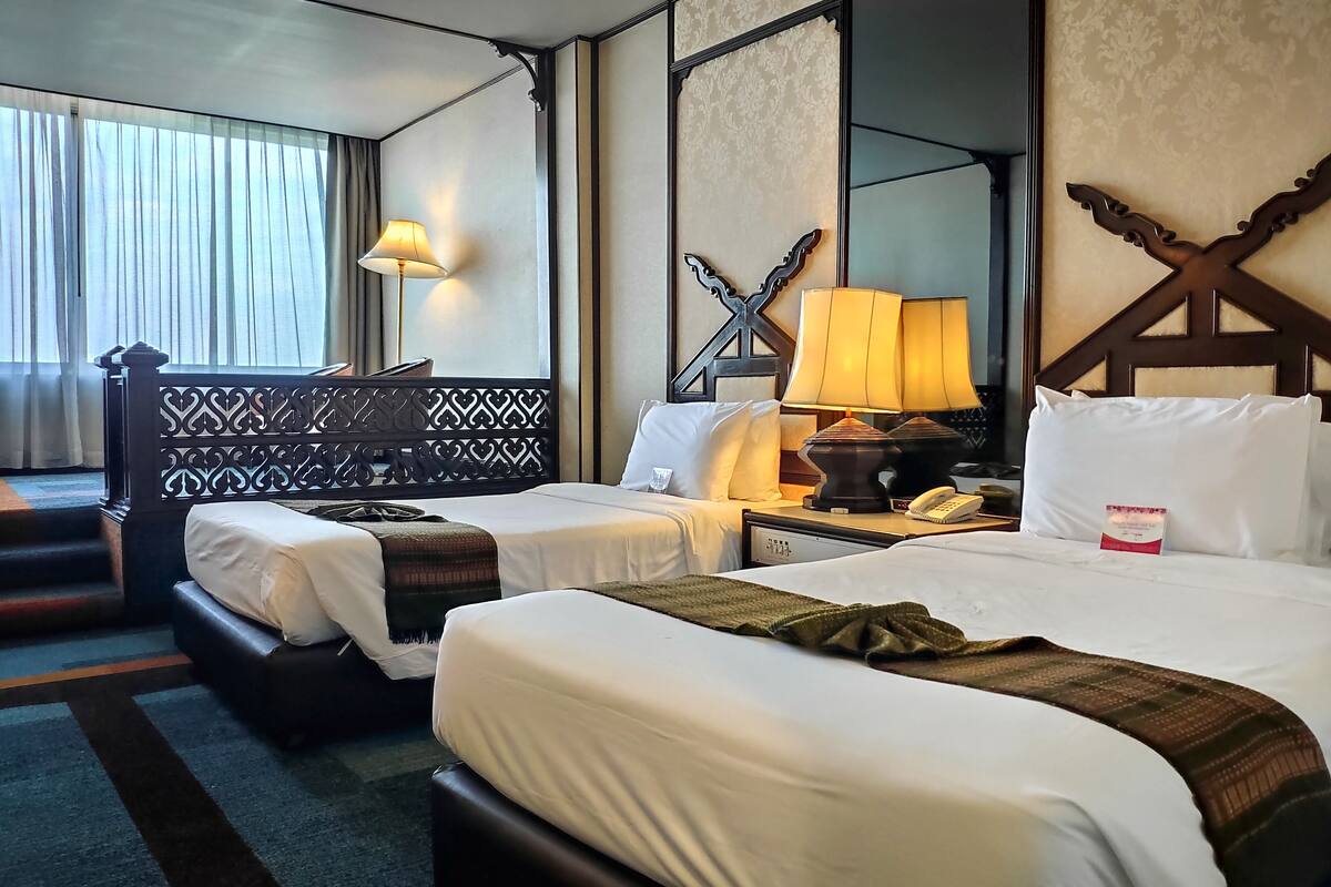Ein Hotelzimmer mit zwei Betten, einem Nachttisch mit Lampe, einem Telefon und einem dekorativen Kopfteil.