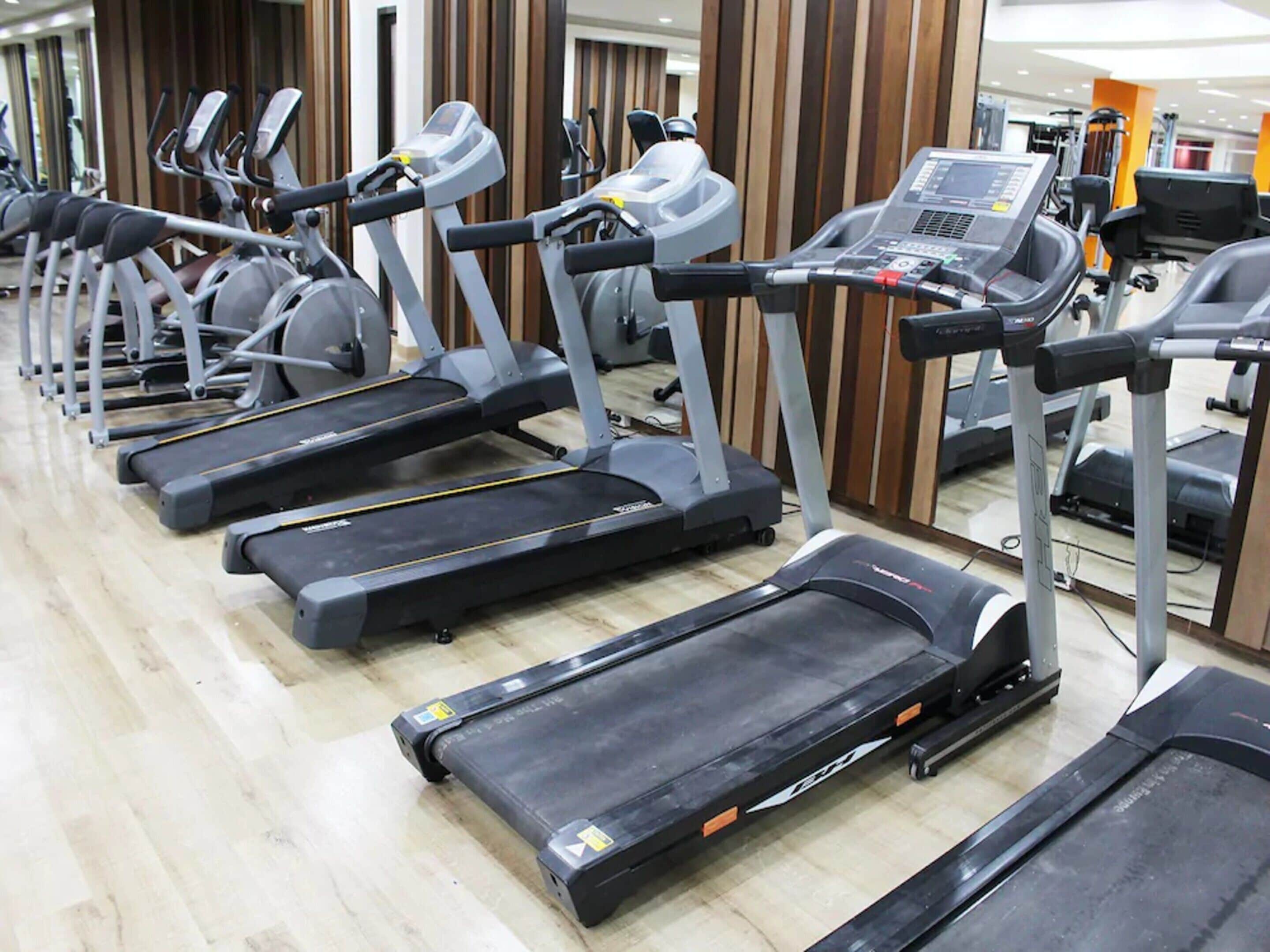 A row of treadmills in a gym with wooden paneling and a mirrored wall.