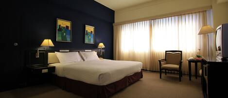 A hotel room with a large bed, two bedside tables with lamps, a chair, a desk with a lamp, and a television.