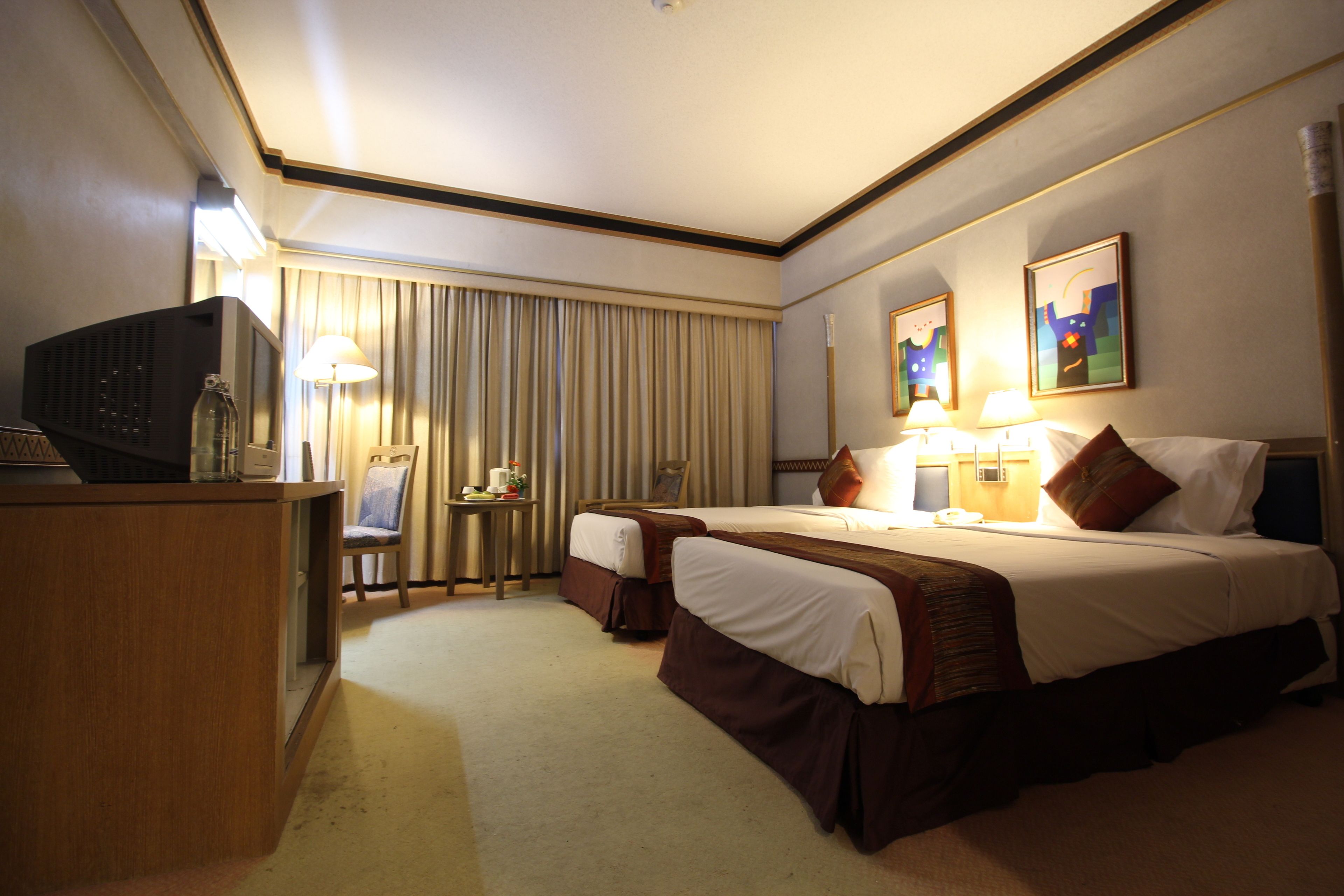 Habitación de hotel con dos camas, un escritorio con televisor, lámparas y obras de arte en las paredes.