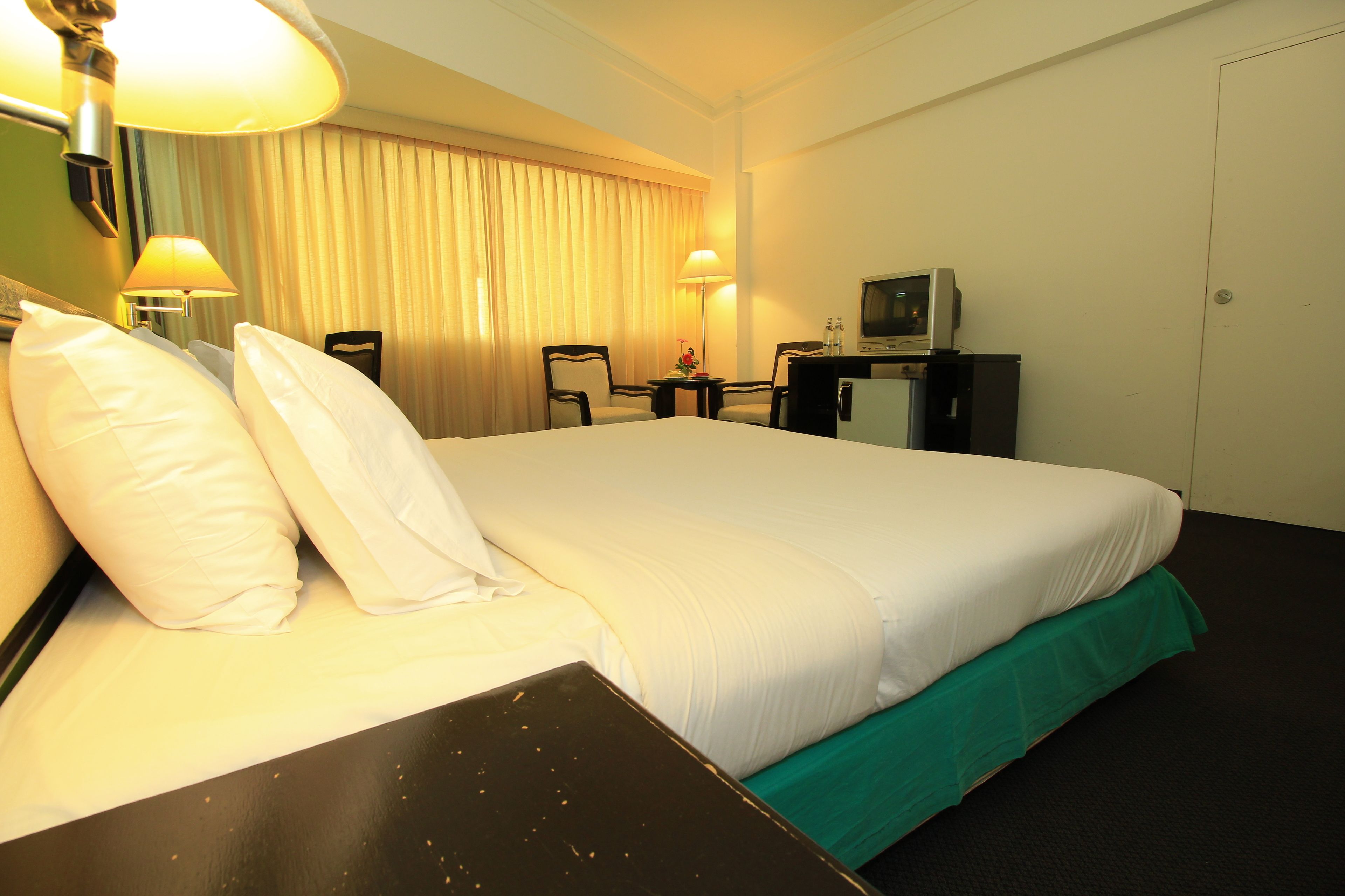 Una habitación de hotel con una cama grande, dos sillas, un escritorio con televisor y una nevera pequeña.