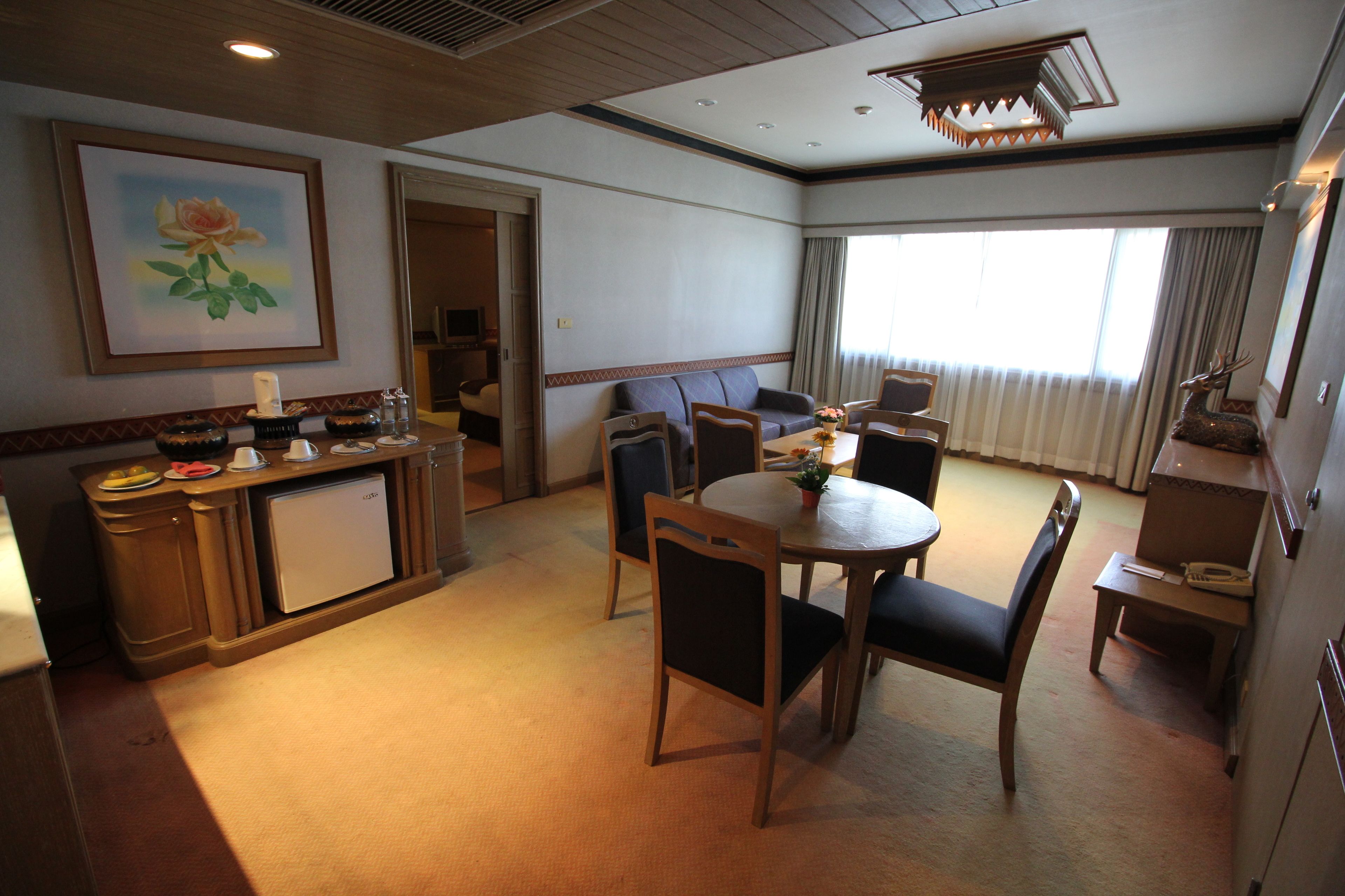 Een hotelkamer met een zithoek, een kitchenette, een bank en een groot raam met gordijnen.